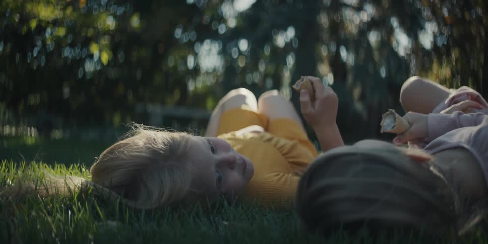 Two little girls laying on the lawn eating an ice cream cone in the summer