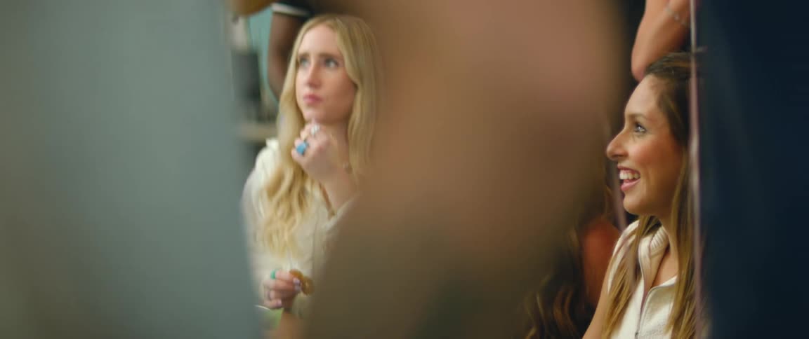Three women with long hair smile as they talk at a celebration while other people stand nearby