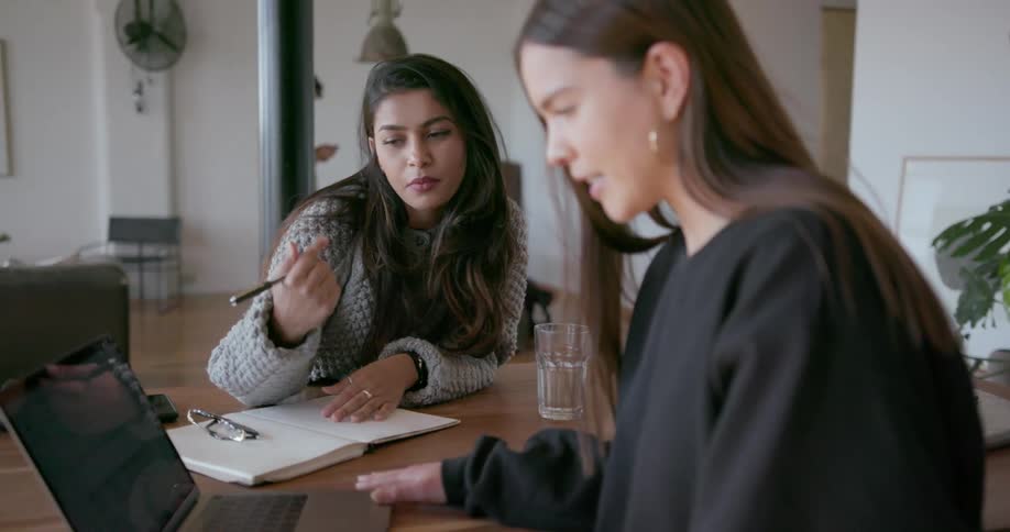 Two women talk while looking at a laptop