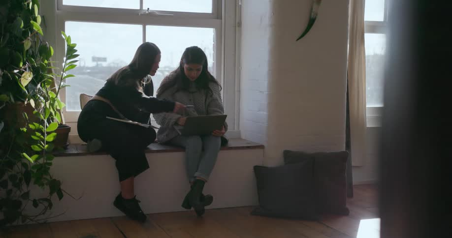 Two people sit on the windowsill working on something together