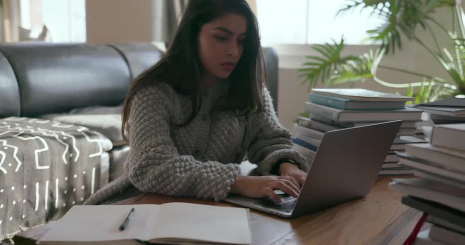 Woman types on a laptop while looking over a notebook