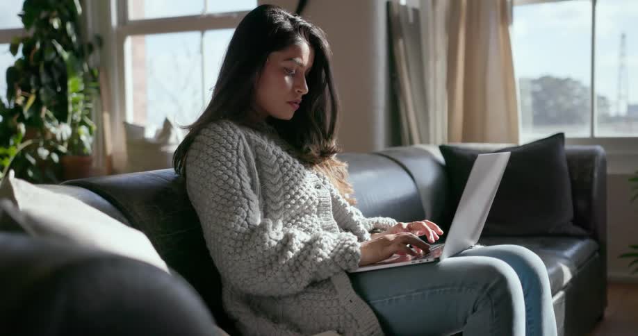 Woman types on a laptop while sitting on a couch