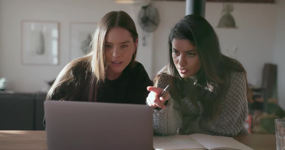 Two women talk and look at a laptop together