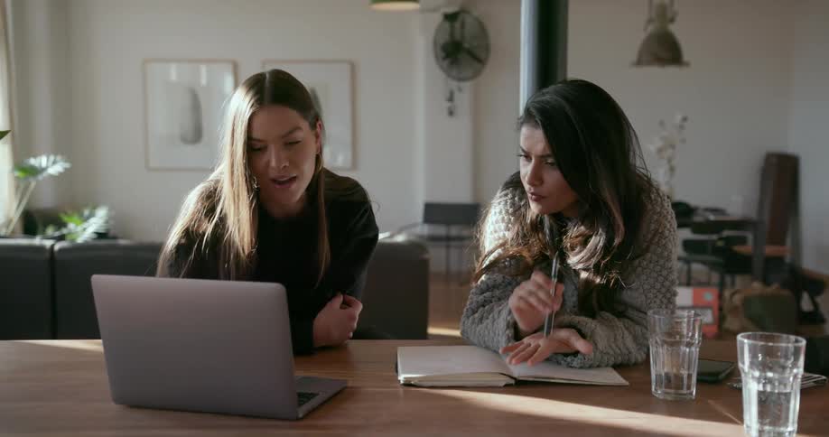 Two women sit down working on school work together