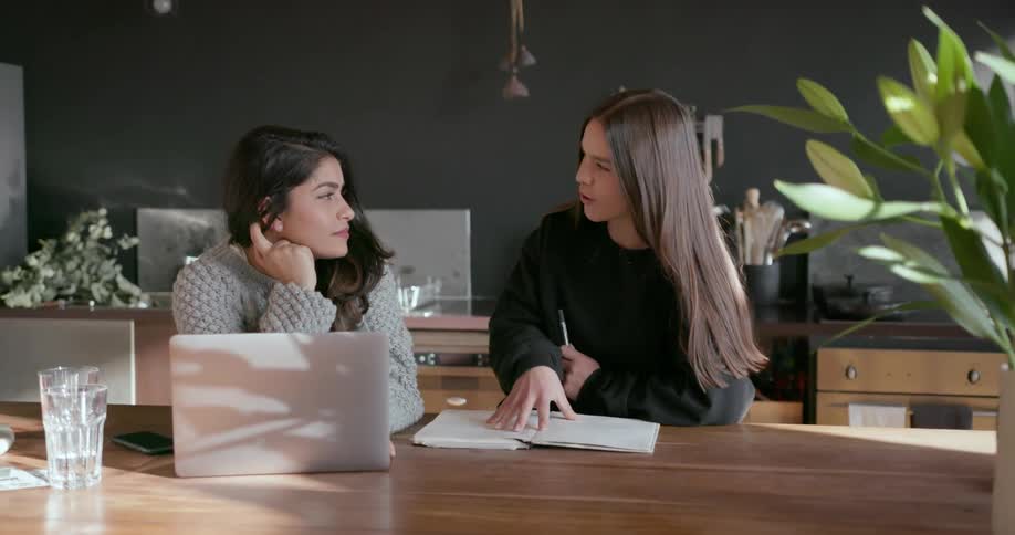 Two women sit at the table together talking