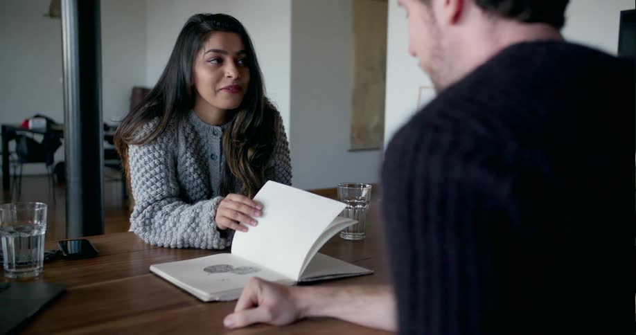 A man and woman talk and look over a book together