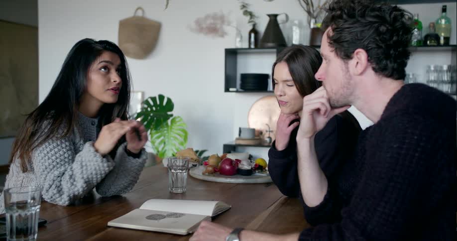 Three people talk and sit at a dining room table
