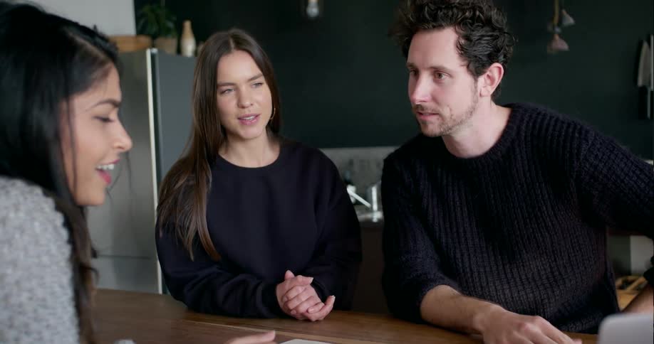 Three people sit around a table talking and pointing towards something