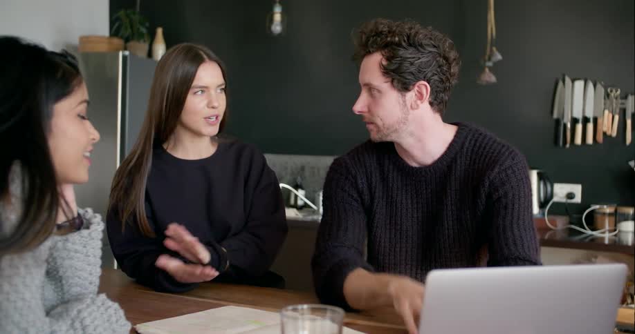 Three people talk and work on a laptop together