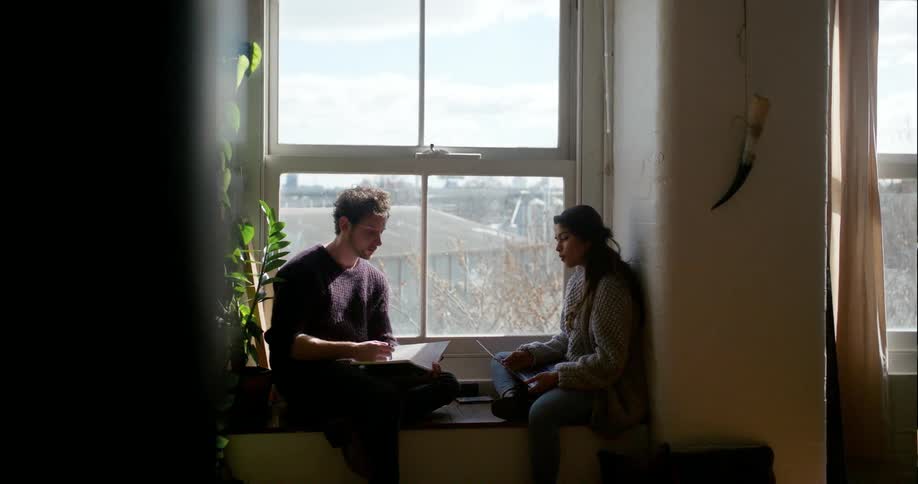 A man and woman sit by the window working on something
