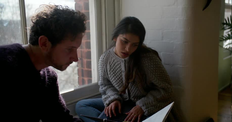 A man and woman lean forward by a window to look at a book