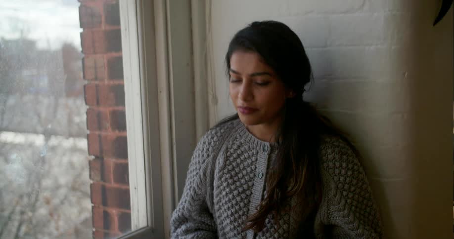 A woman types on her keyboard and talks with another person near the window
