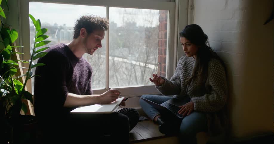 A man and woman have a conversation sitting by a window