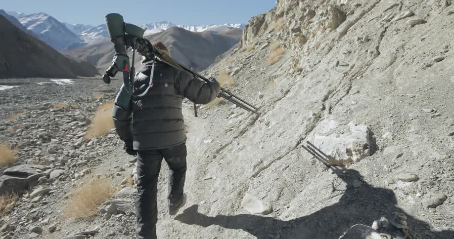 A man in a puffy jacket walks over stones