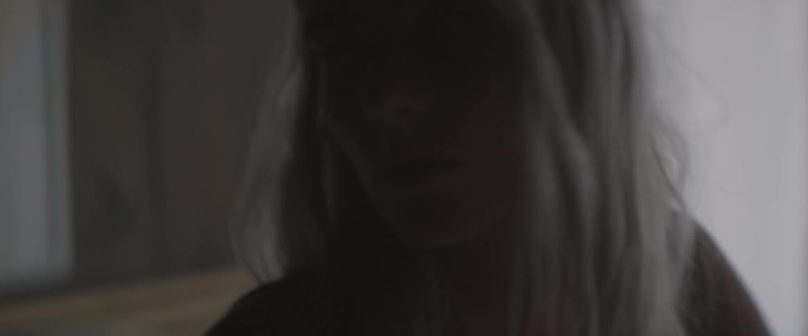 A blond woman puts her hair behind her ears and looks around her room