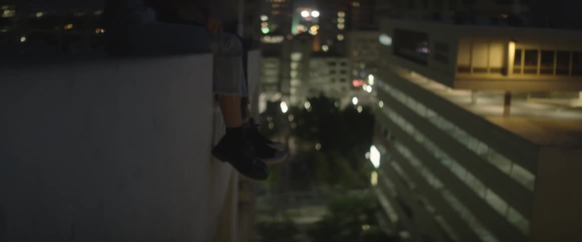 Man and woman sitting at the edge of a building at night
