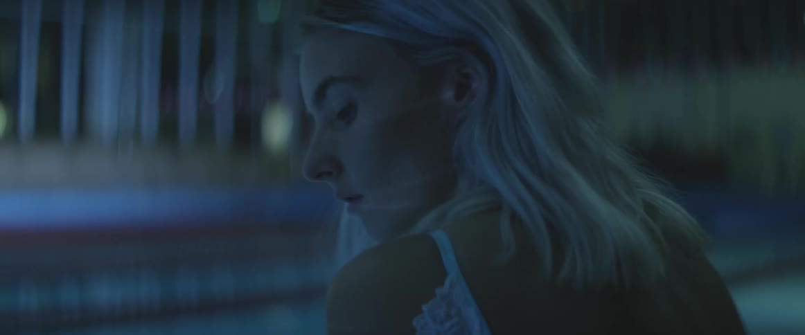 A woman is sitting at night by a pool