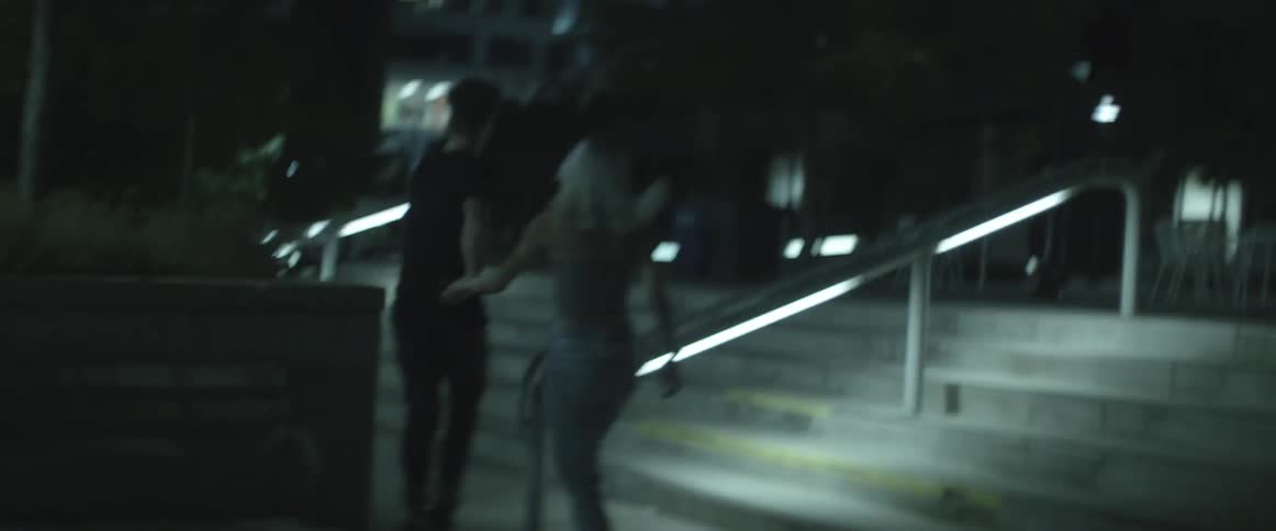 A man and women run at night up steps and past buildings