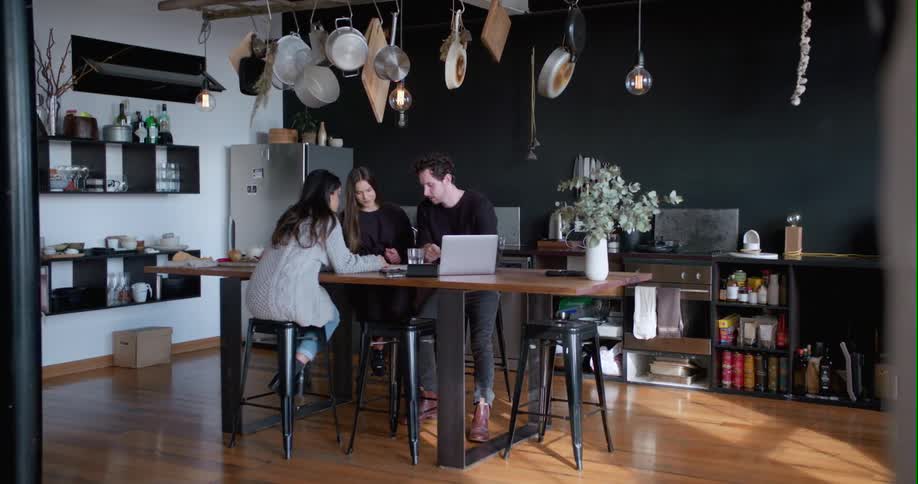 Friends are gathered around a laptop and notebook in a kitchen