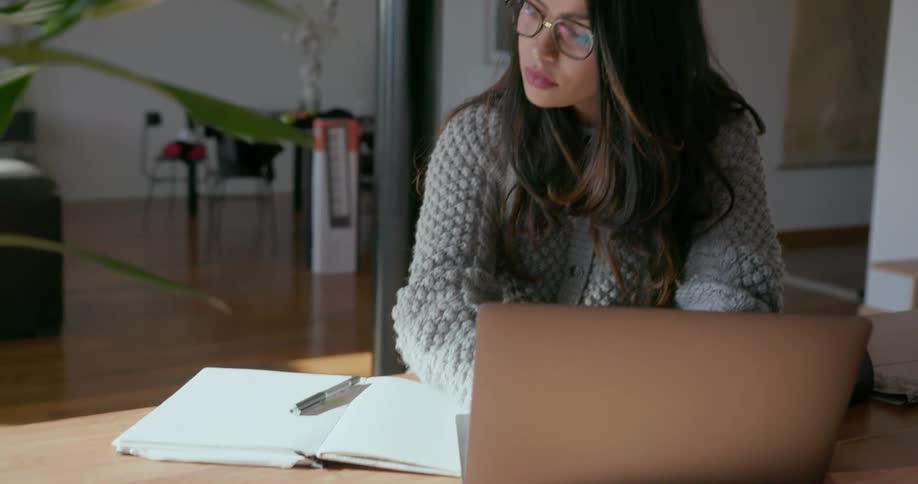 Woman types on her laptop as she glances at a notebook
