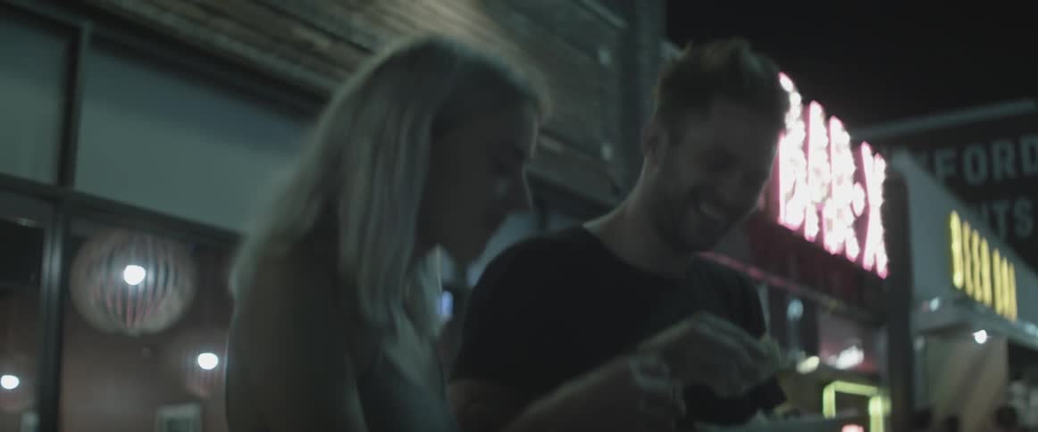 A man and women laugh and eat outside at night