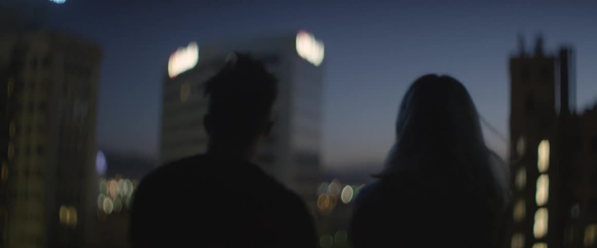 A man and woman look out over a balcony on a city at night