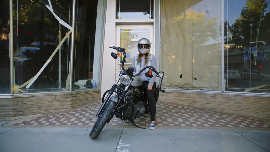 Female biker with sunglasses silver helmetdenim jacket and black pants poses for the camera