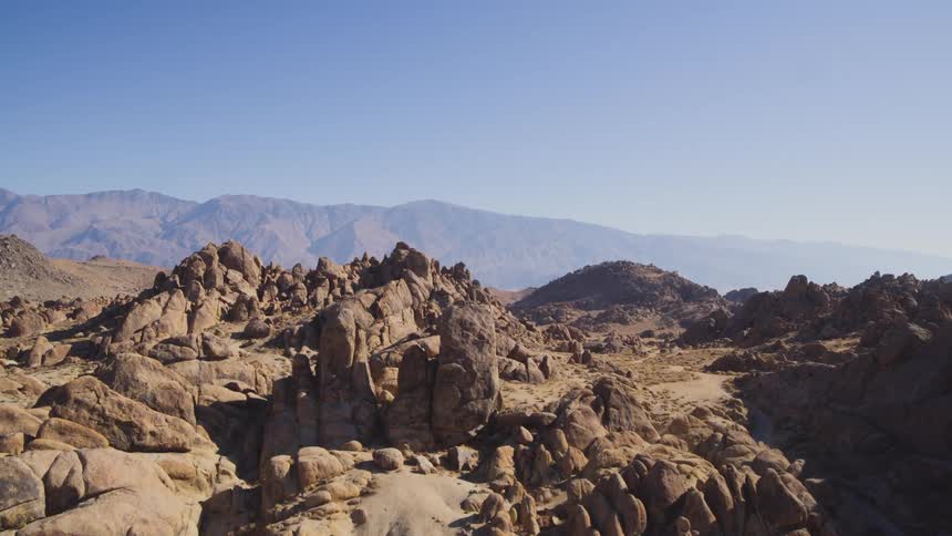 Dirt trails wind through rough boulder strewn terrain toward mist covered mountains
