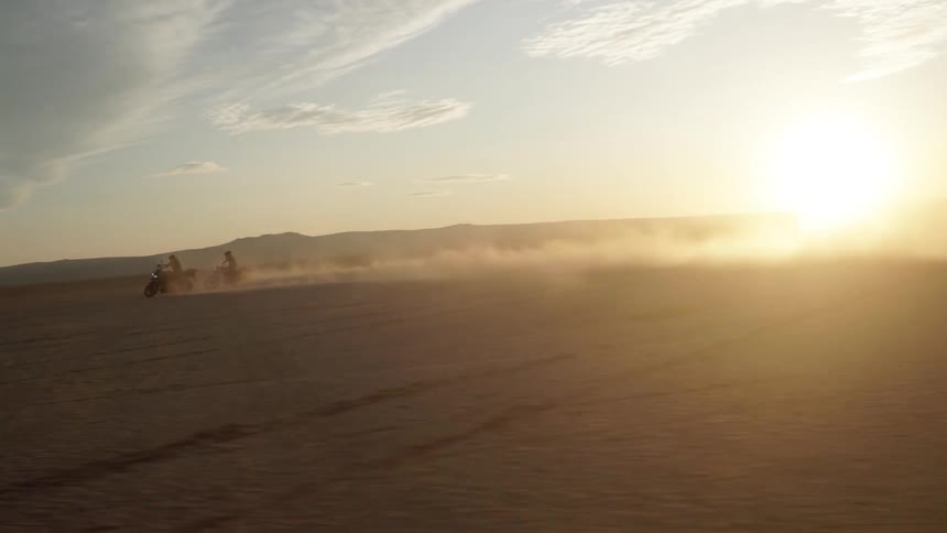 Bikers with motorcycle helmet jacket and pants skids across desert at sunset