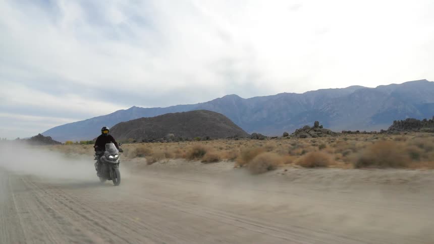 Two people ride motorcycles down a dirt road