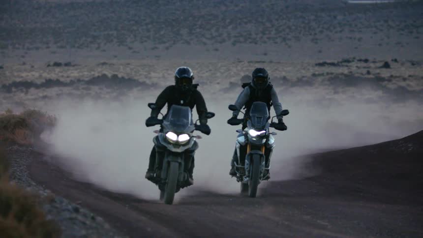Bikers with motorcycle helmets black jacket and pants ride motorcycles uphill on dirt road at dusk