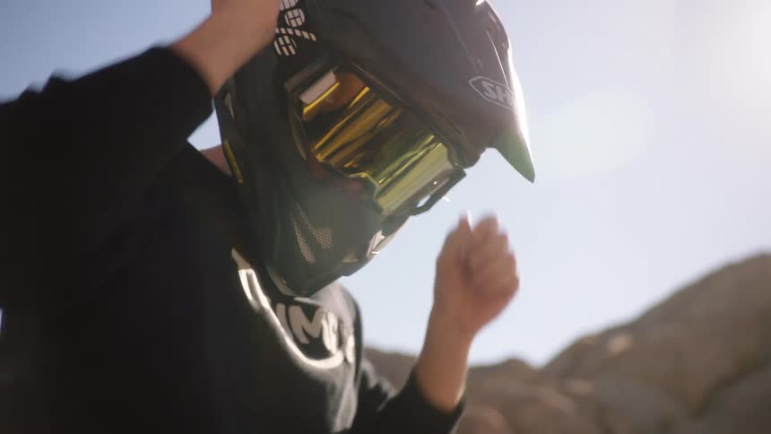 Male biker with black sweatshirt and motorcycle helmet puts on googles in the desert