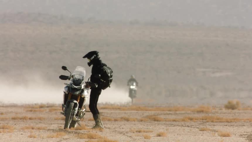 A person is getting on a motorcycle in the desert