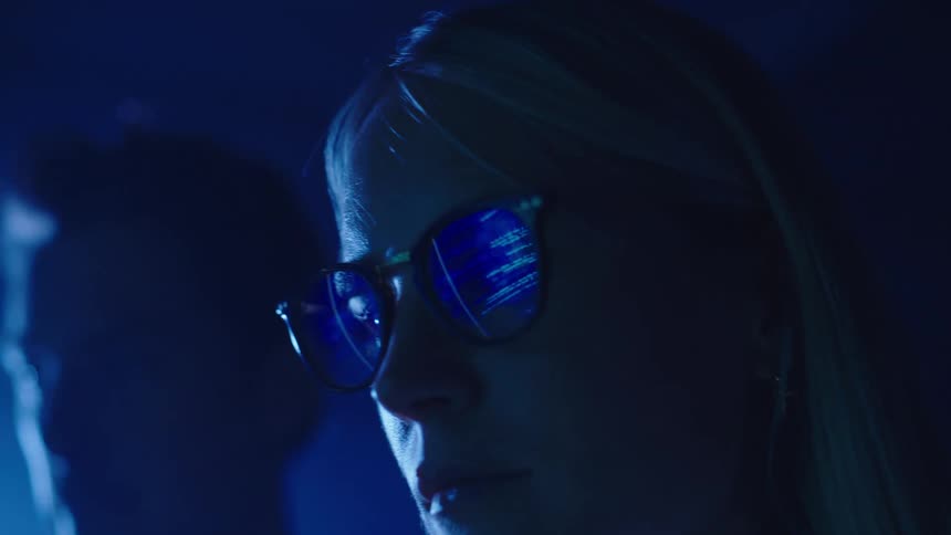 Display screen with text on it reflects in a womans glasses as a man sits next to her