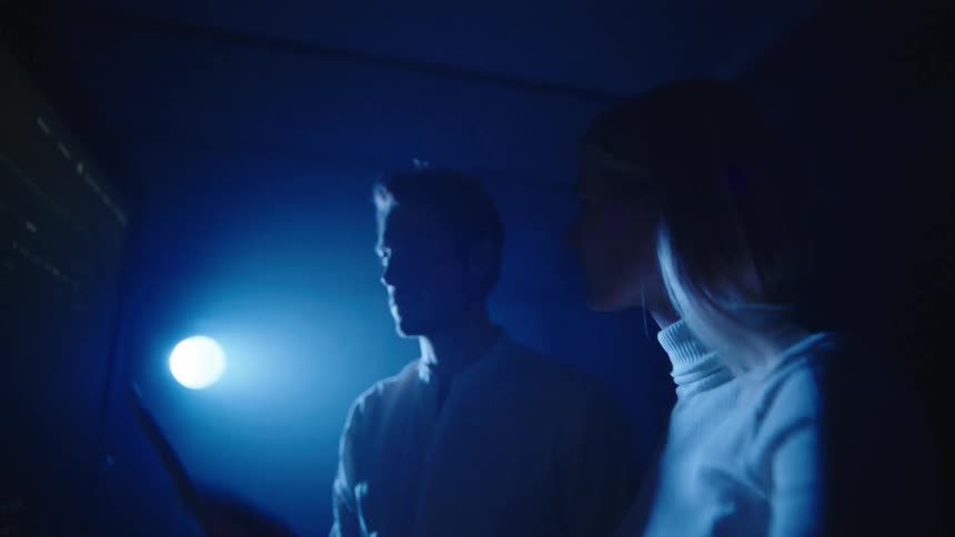 Two people are looking at a screen in a dark room