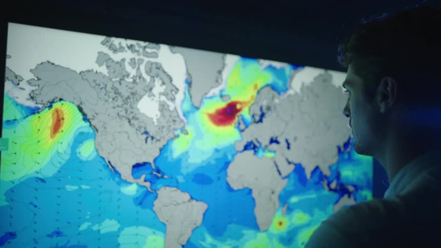 Man stand in front of large television screen showing weather data in a dark room lit by a bright light