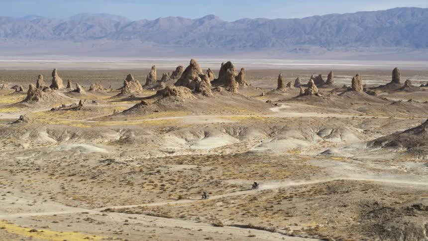 Two people ride dirt bikes in the desert