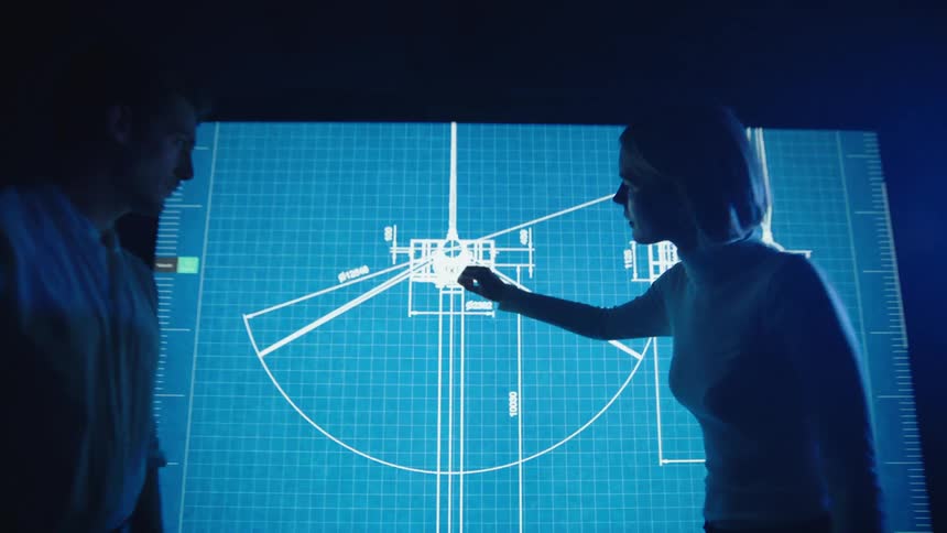 Woman uses her hand to scroll on a large touch screen monitor as a man stands nearby and watches