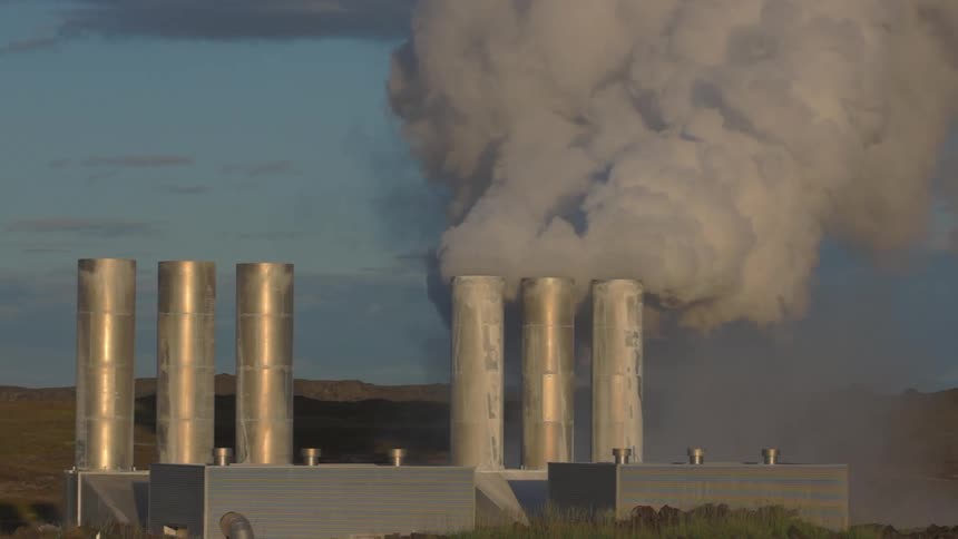 Smoke rises from chimneys at factory near mountains as birds fly around