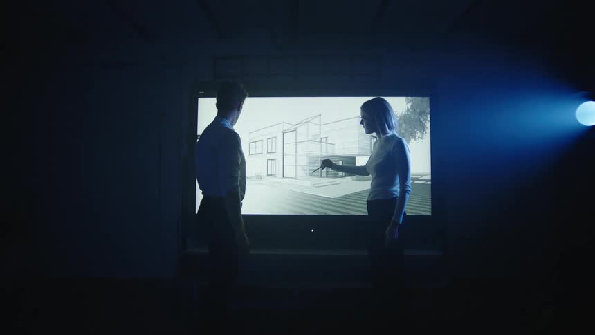 A man and woman look at architecture designs on the projector screen