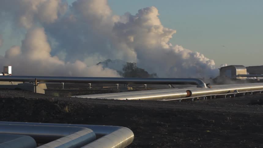 Heavy smoke rises from metal pipes in a field of crops