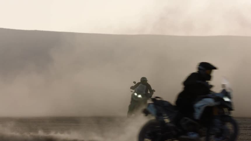 Two people are riding motorcycles on gravel at dusk