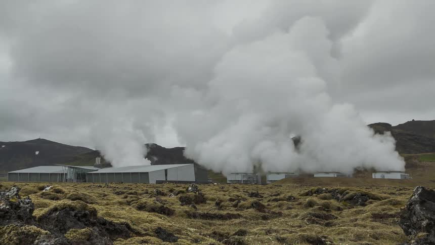 Smoke billows from the buildings in a field near the mountains under a cloudy sky
