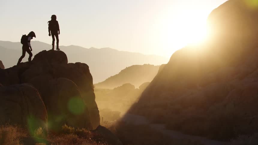 Two men climb to the top of a narrow peak in a canyon