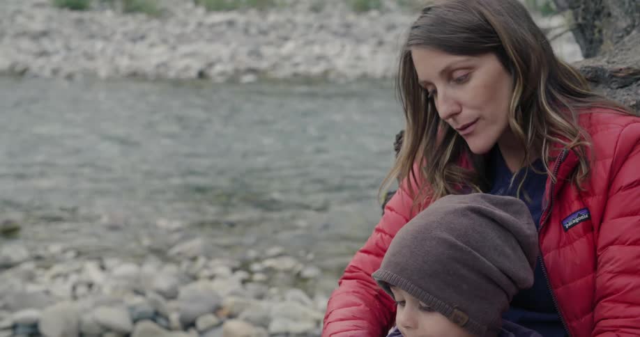 Mother and son sit near tree on river bank reading a book together