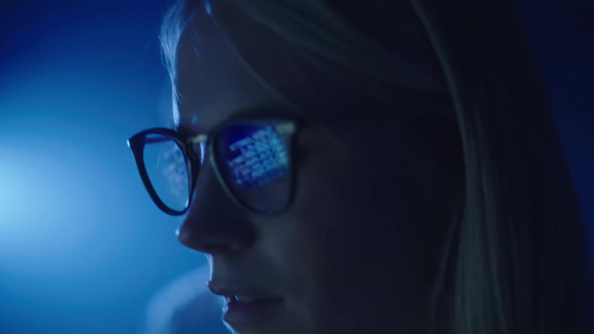 The reflection in a womans glasses show her reading lines of code on a computer