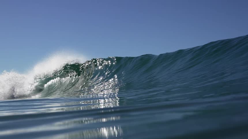 Large ocean wave rolling and splashing under a blue sky