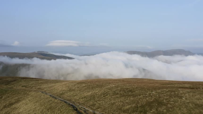 Field and mountains surround the white mist under a blue sky
