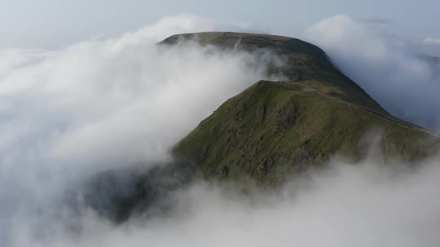 Aerial view of the top of a mountain surrounded by thick white clouds at evening