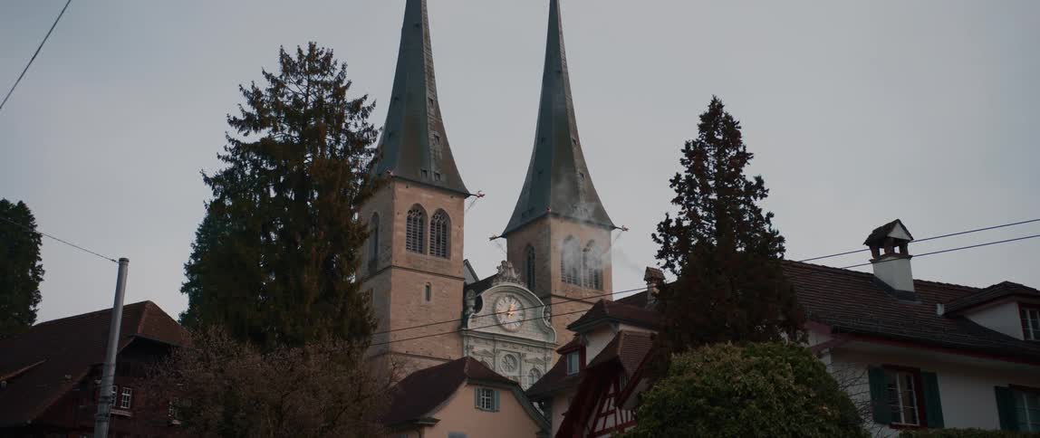 White smoke from a chimney in front of a big clock in the facade of a building with towers